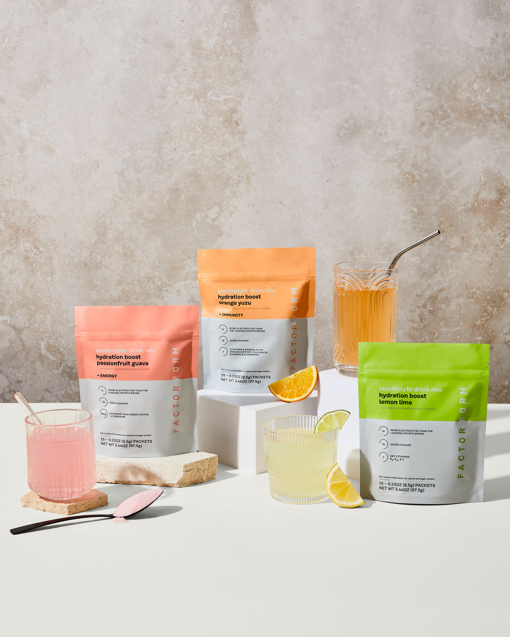 Packages of a beverage mix with glasses of prepared drinks on a neutral background