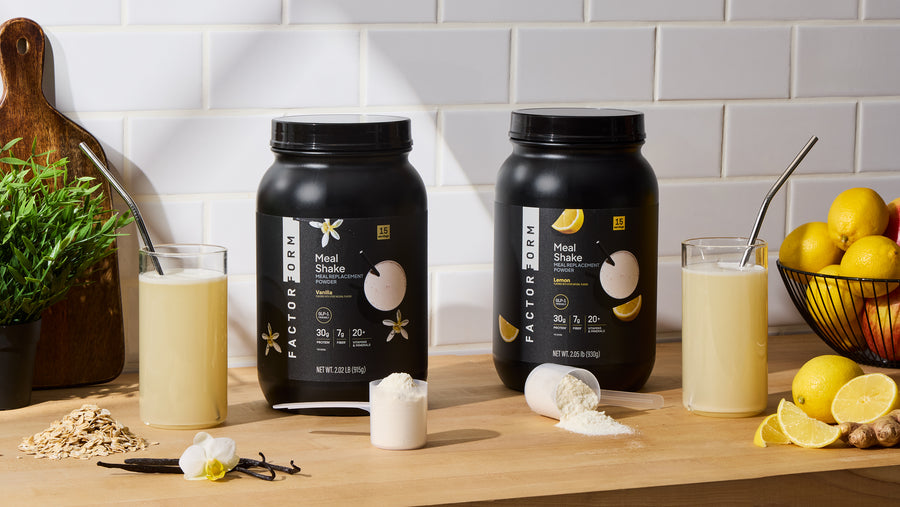 Two containers of Factor Form meal shake on a wooden surface with glasses of shake and lemons.